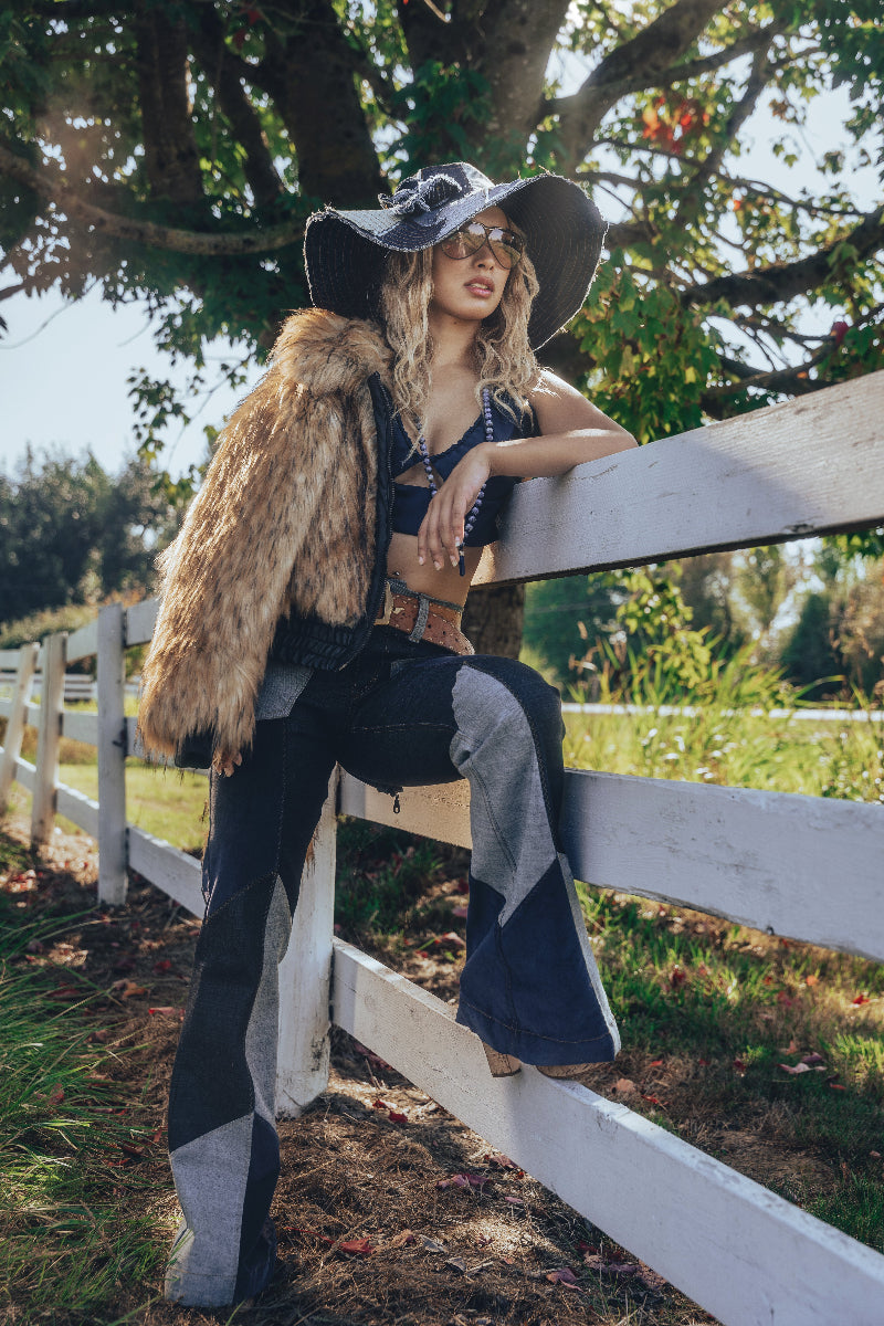 Woman wearing 70s inspired patchwork bell bottom jeans a denim halter top and a wide brim patchwork denim hat styled with retro flair and soulful attitude