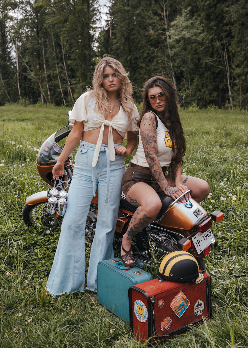 Girl sitting on the floor wearing a denim waistcoat and high-waisted 1970s-style bell-bottom jeans, showcasing retro 70s fashion, vintage-inspired denim, and sustainable small-batch style.