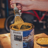 Hand holding a paintbrush over a can of yellow paint on a wooden surface.