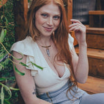 Woman with red hair sitting outdoors on wooden steps surrounded by plants
