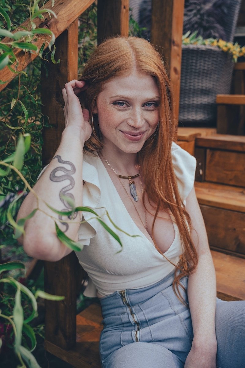 Woman with red hair sitting outdoors among plants