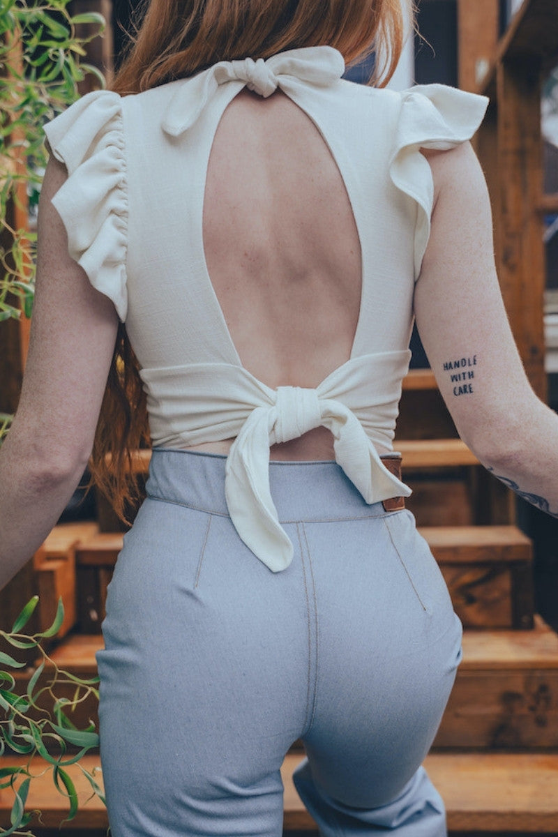 Person wearing a white top with an open back and light gray pants outdoors.