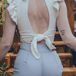 Person wearing a white top with an open back and light gray pants outdoors.