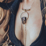 A person wearing a gold-plated chain necklace with a teardrop-shaped pendant that drapes over the chest.