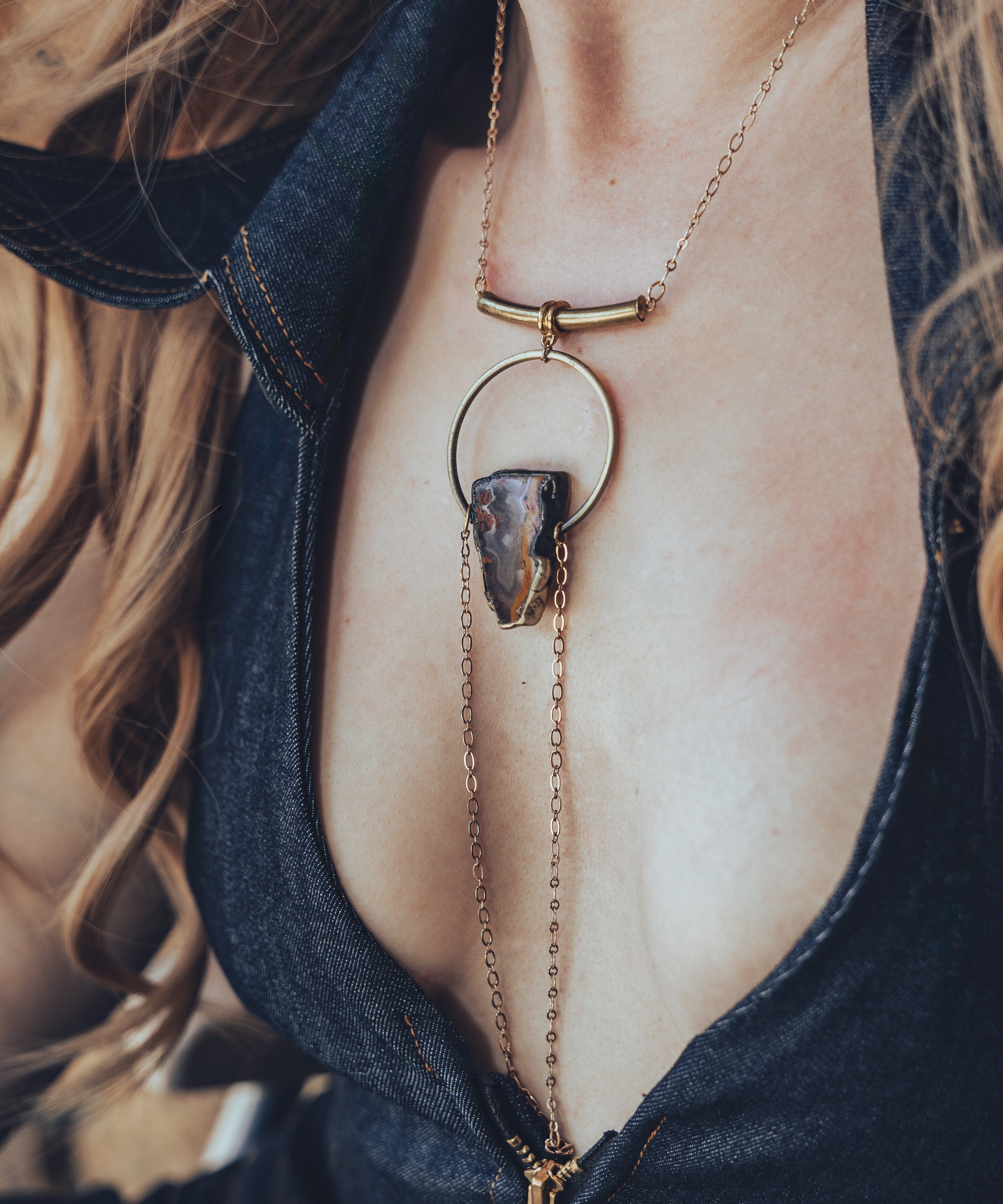 A person wearing a gold-plated chain necklace with a teardrop-shaped pendant that drapes over the chest.