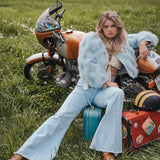 Woman sitting on a suitcase next to a motorcycle in a grassy field wearing Soul Sister since 1969
