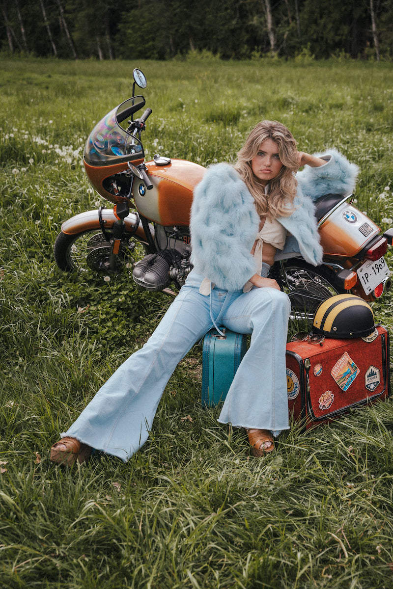 Woman sitting on a suitcase next to a motorcycle in a grassy field wearing Soul Sister since 1969