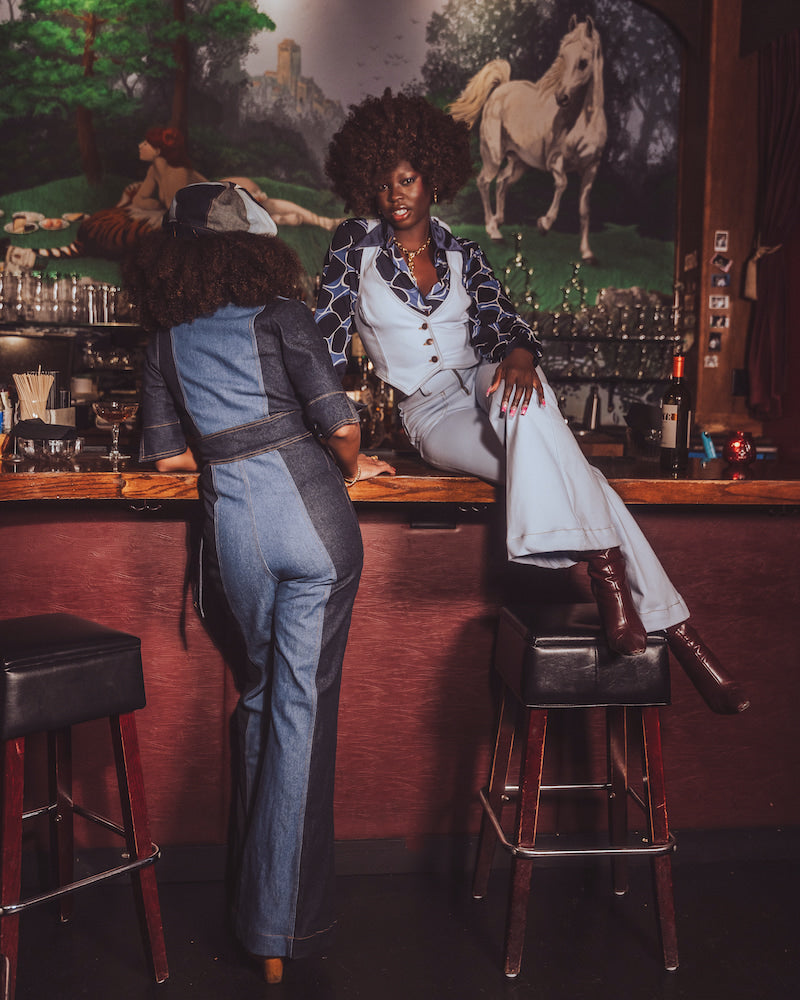Two women in vintage clothing sitting at a bar with horse mural in the background