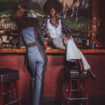 Two women in 1970s vintage clothing sitting at a retro speakeasy bar with horse mural in the background