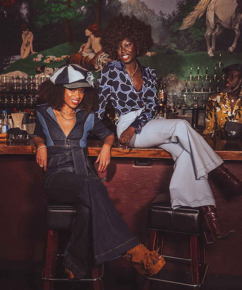 Two women sitting at a bar with a vintage painting in the background