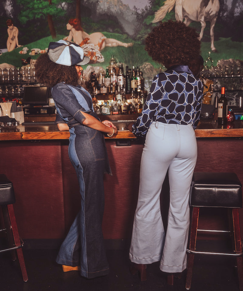 Two people standing at a bar with a vintage mural in the background