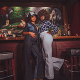 Two women posing in a bar with a painting of a picnic scene on the wall.
