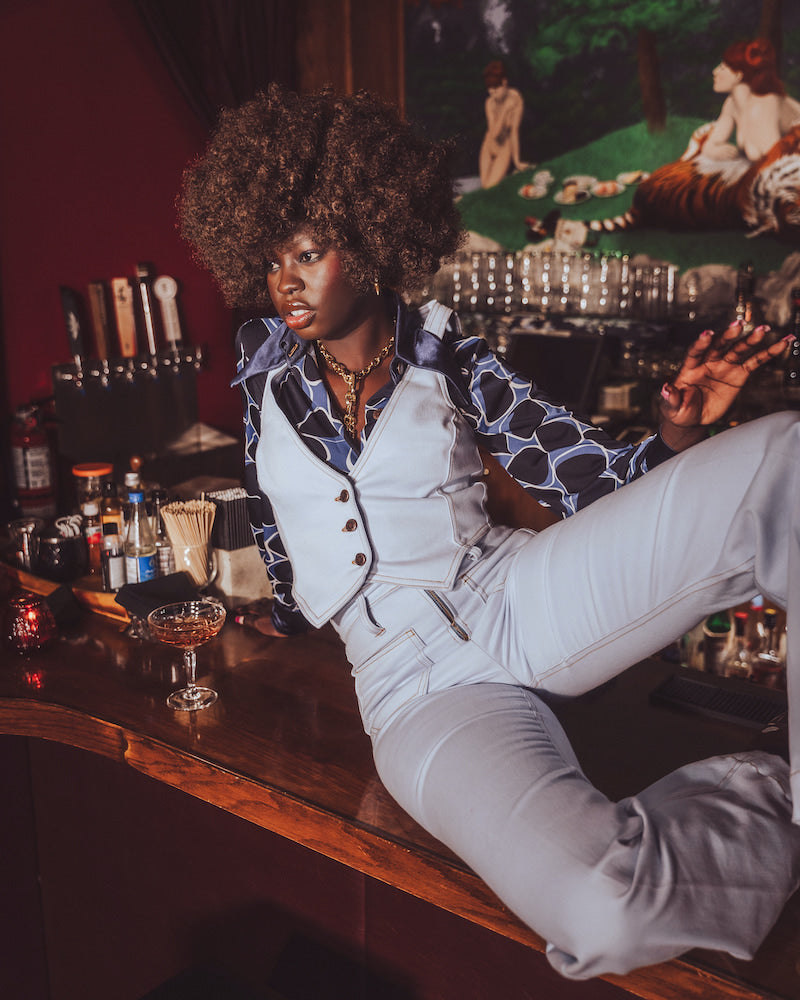 Woman sitting at a bar counter in a stylish outfit with a dark background