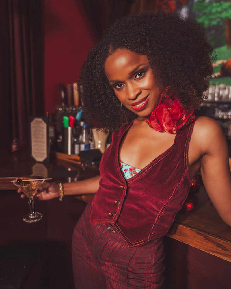 Woman in a sexy red  1970s inspired velvet outfit holding a cocktail at a retro speakeasy bar.