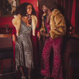 Two women in glamorous  studio 54 style outfits with fur coats standing in a r1970s style speakeasy bar