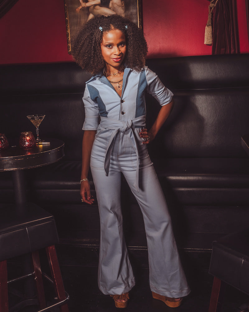 Woman in a light blue jumpsuit standing in a bar setting