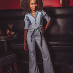 Woman in a light blue jumpsuit standing in a bar setting