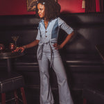 Woman in a gray jumpsuit standing in a bar with a painting on the wall.