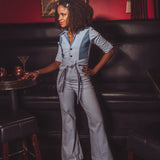 Woman in a gray jumpsuit standing in a bar with a painting on the wall.