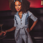 Woman in a gray jumpsuit standing in a bar setting with a drink tray.