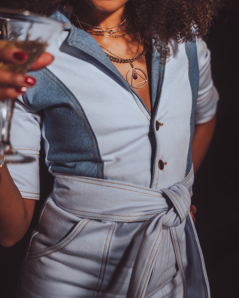 Person wearing a light blue outfit with a belt, holding a glass.