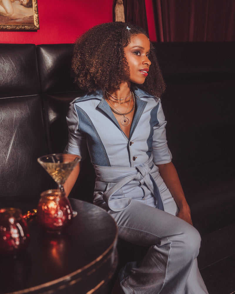 Woman in a gray outfit sitting on a dark leather couch with candles on a table.