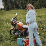 Woman in a light blue outfit standing next to a motorcycle in a grassy field Soul Sister since 1969..