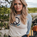 Woman wearing a t-shirt with a logo and text, standing outdoors with greenery and a motorcycle in the background Woman wearing a peace symbol shirt with text outdoors wearing Soul Sister since 1969.