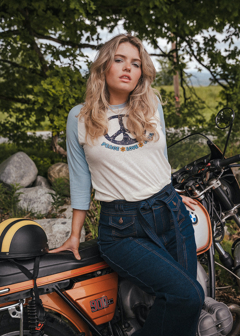 Woman sitting on a motorcycle wearing a peace sign t-shirt with a scenic background Woman wearing a peace symbol shirt with text outdoors wearing Soul Sister since 1969