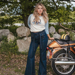 Woman standing next to a motorcycle in a natural setting with trees and rocks wearing Soul Sister since 1969..