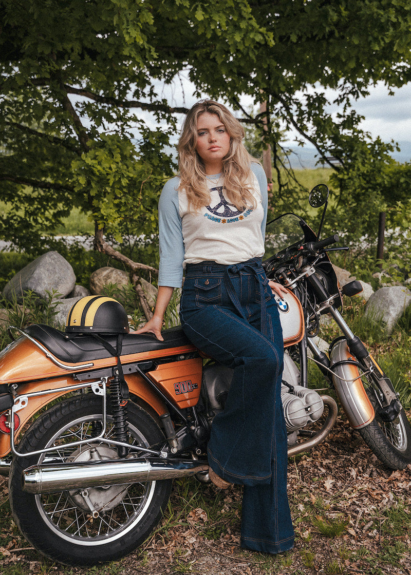 Woman sitting on a motorcycle in a natural setting with trees and rocks wearing Soul Sister since 1969..