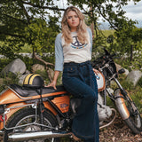 Woman sitting on a motorcycle in a natural setting with trees and rocks wearing Soul Sister since 1969..