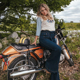 Woman sitting on a motorcycle in a natural setting with trees and grass wearing Soul Sister since 1969..