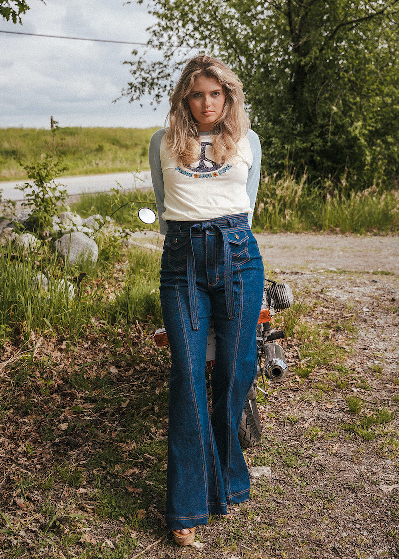 Woman in a white t-shirt and blue jeans standing next to a motorcycle in a natural setting wearing Soul Sister since 1969..