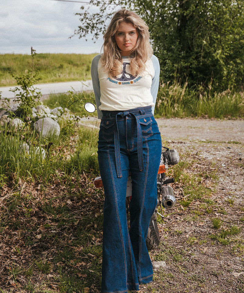 Woman in a white t-shirt and blue jeans standing next to a motorcycle in a natural setting wearing Soul Sister since 1969..