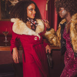 Two women in glamorous 70s disco inspired outfits with fur collars in a retro vintage setting.