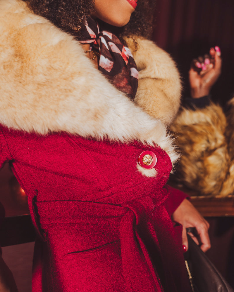Close-up of a person wearing a red vintage inspired 1970s coat with fur trim and a floral scarf.