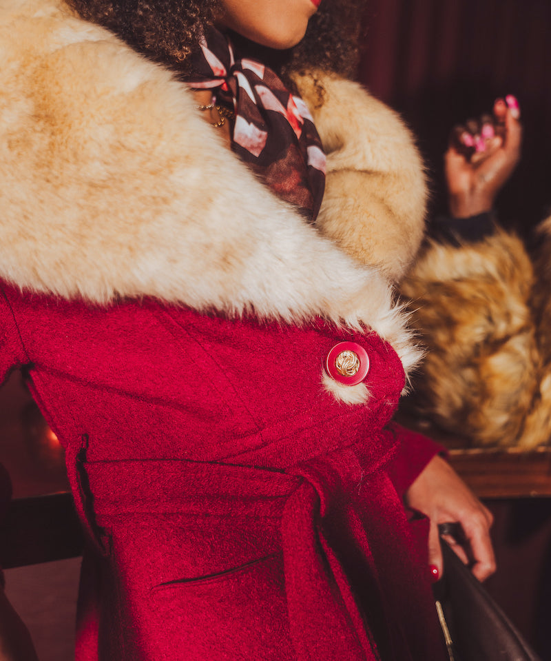 Close-up of a person wearing a red vintage inspired 1970s coat with fur trim and a floral scarf.