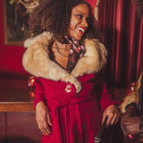 Woman in a red 1970s inspired coat with fur collar standing in a retro speakeasy bar  with red walls and curtains.