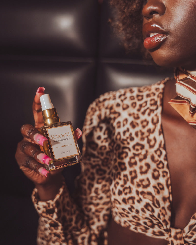 Woman in leopard print outfit holding a perfume bottle with a dark background