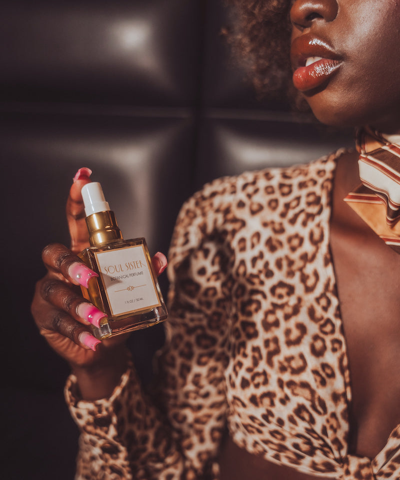 Woman in leopard print outfit holding a perfume bottle with a dark background