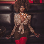 Woman in leopard print top and red pants sitting on a black leather couch with a red wall and painting in the background.