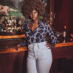 Woman standing in a 1970s disco  bar wearing a funky vintage inspired groovy shirt with a decorative mural in the background
