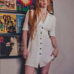 Woman in a white dress standing in front of a wall with vintage posters.