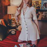 Woman in a white dress standing in a room with posters on the wall