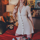 Woman in a white dress standing in a room with posters on the wall