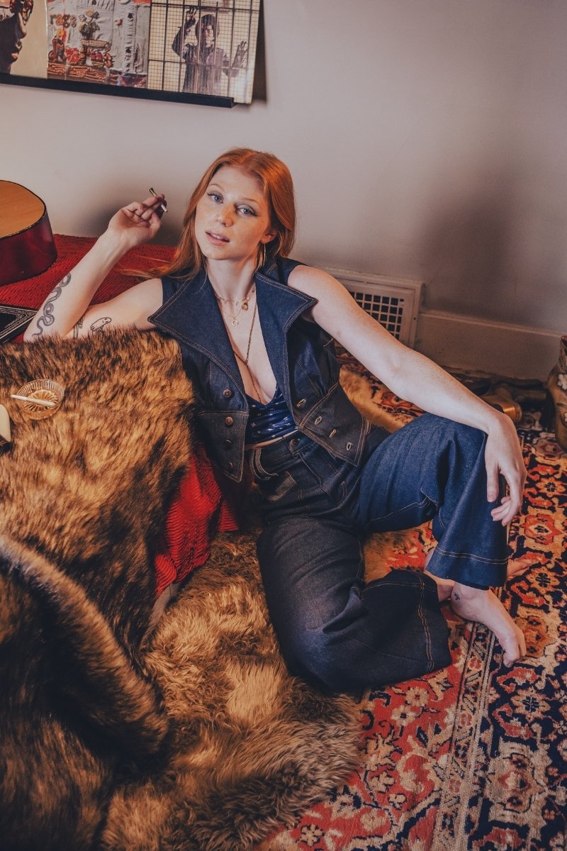 Woman sitting on a patterned rug in a room with a guitar and wall art.