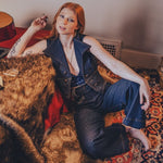 Woman sitting on a patterned rug in a room with a guitar and wall art.