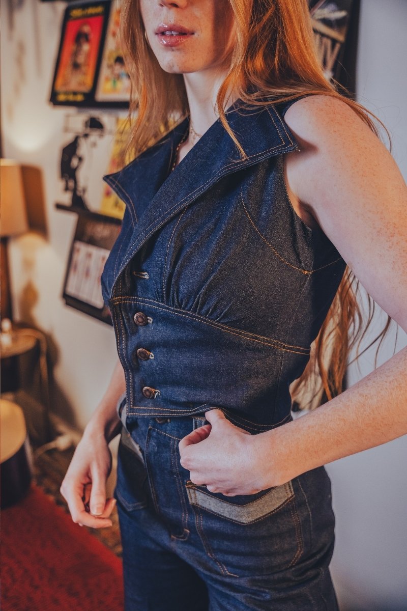 Person wearing a funky 70s inspired denim vest and high waisted bellbottom jeans in an indoor setting with decor.