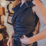 Person wearing a funky 70s inspired denim vest and high waisted bellbottom jeans in an indoor setting with decor.